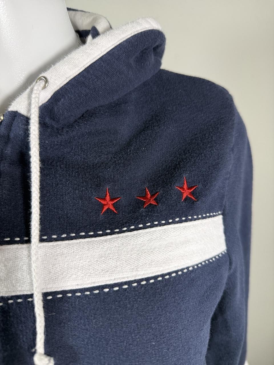 Y2K Studio Norton navy zip-up hoodie featuring sporty white stripe details, red embroidered stars, and a cozy hood with adjustable drawstrings. A classic early 2000s layering piece that's perfect with jeans, cargos, or athleisure looks.